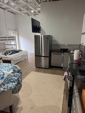 A modern kitchen with stainless steel appliances, a bed with patterned bedding, and a view of the outdoors.