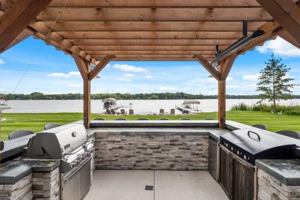 An outdoor barbecue area with stone and wood features, overlooking a lake.