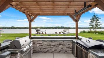 An outdoor barbecue area with stone and wood features, overlooking a lake.