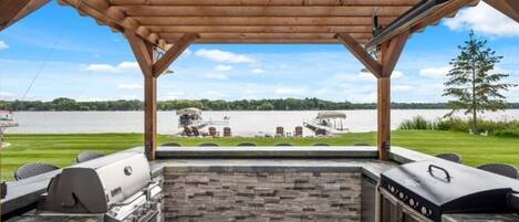 An outdoor barbecue area with stone and wood features, overlooking a lake.