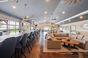 A spacious indoor area with a long dining table, multiple chairs, a sofa, and a coffee table. - Spacious Lakefront Retreat, with Room for Everyone. Cabin and Event Center. (Isanti)