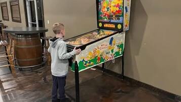 A child playing a pinball machine in a room with a wooden barrel and a door in the background.