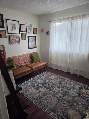 Ein Wohnzimmer mit einem braunen Ledersofa, einem gemusterten Teppich und verschiedenen gerahmten Kunstwerken an der Wand.