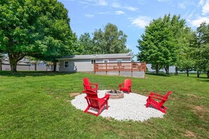 A backyard with a fire pit, red Adirondack chairs, and a wooden deck.