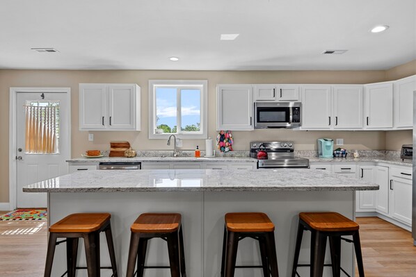 A modern kitchen with white cabinets, a central island with bar stools, stainless steel appliances, and a window with a view.