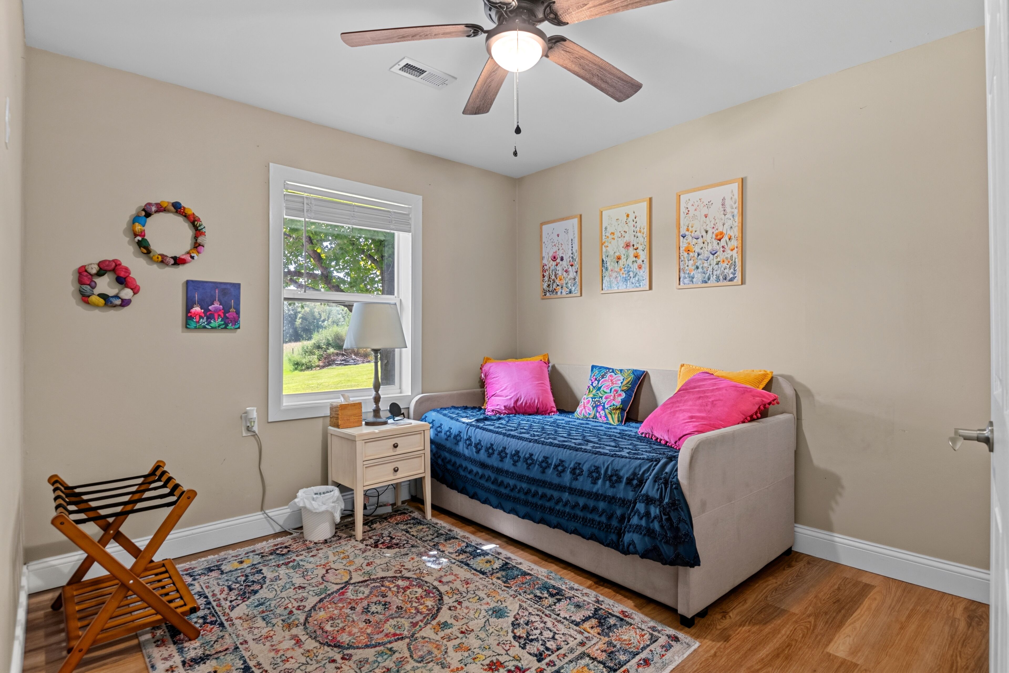 A bedroom with a bed, a nightstand, a lamp, a chair, a window, and wall decorations.
