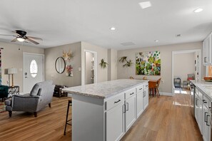 A modern kitchen with a central island, wooden flooring, and a dining area with a chair and table.