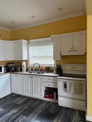 A kitchen with white cabinets, a microwave, a coffee maker, a sink, and an oven. - A Cozy Stay on Coronation Street (St. John's)