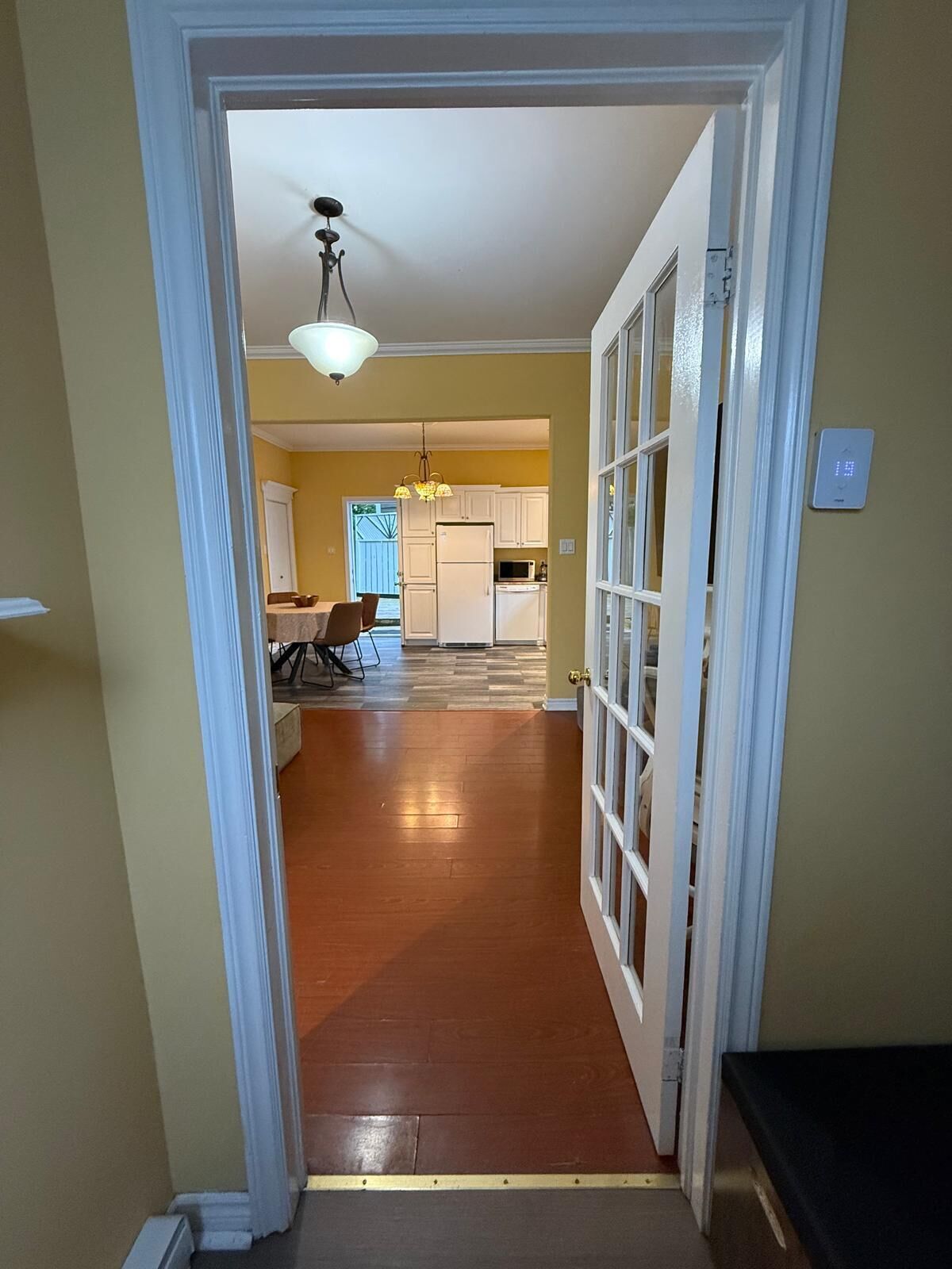 A hallway leading to a dining area with a table and chairs, a kitchen with cabinets and appliances, and a ceiling light fixture.