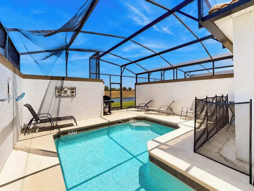 A covered outdoor swimming pool with lounge chairs and a barbecue grill.