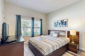 Ein Hotelzimmer mit Bett, Schreibtisch mit Fernseher und Fernbedienung, Fenster mit Vorhängen und einem Wandbild.