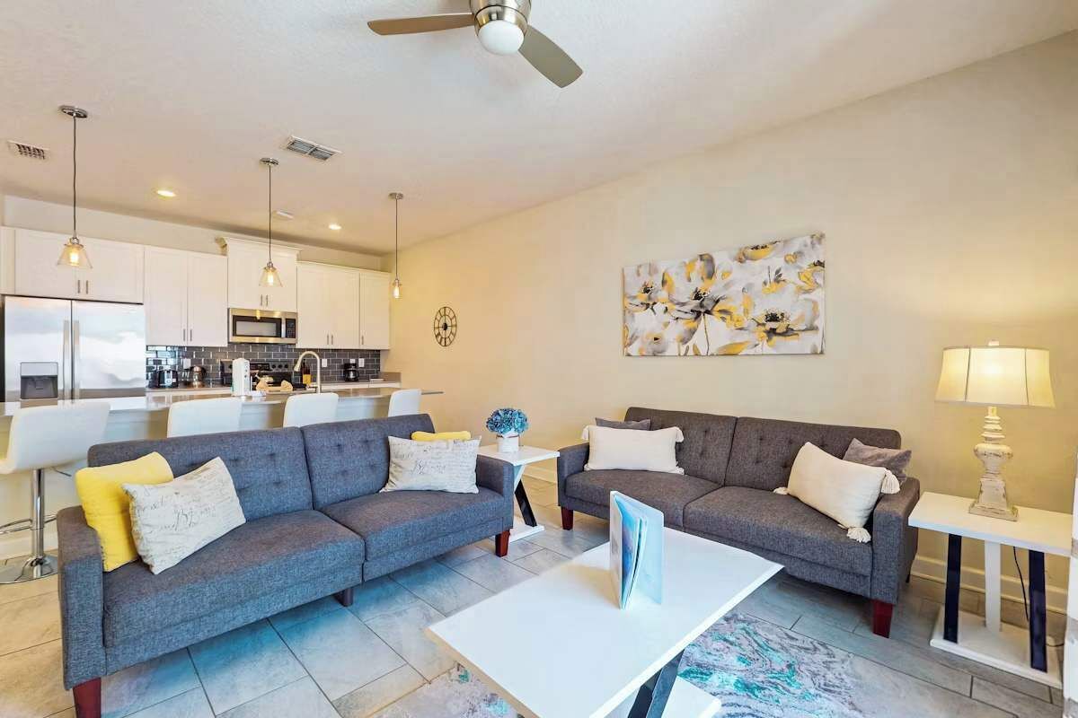 A modern living room with grey sofas, a white coffee table, and a kitchen in the background.