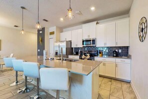 A modern kitchen with white cabinets, stainless steel appliances, and a central island with bar stools. - Pet-Friendly 4BR Near Disney - Private Heated Pool & Resort (Davenport)