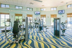 Ein Fitnessstudio mit verschiedenen Trainingsgeräten, großen Fenstern und einem gemusterten Teppich.