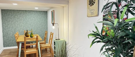 Un coin repas avec une table et des chaises en bois, un mur orné d’un motif vert et une plante en pot.