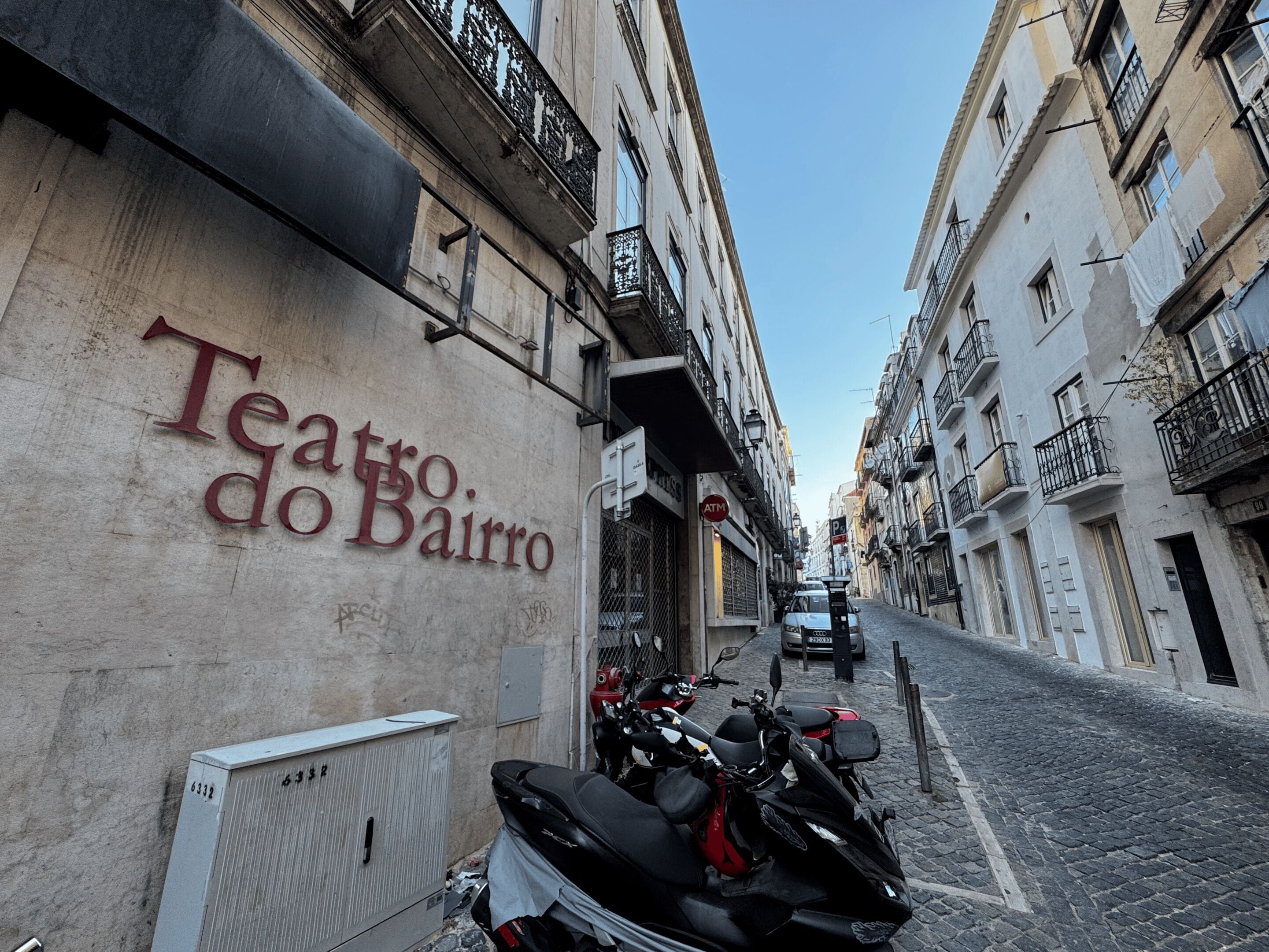 A narrow street with a building labeled 'Teatro do Bairro' and parked motorcycles.