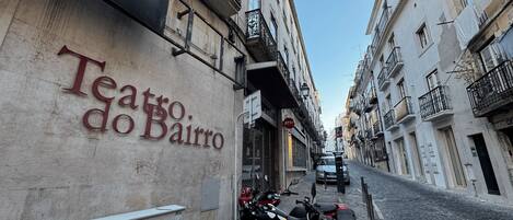 A narrow street with a building labeled 'Teatro do Bairro' and parked motorcycles.