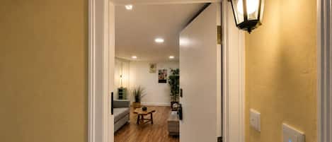 Un pasillo que conduce a una sala de estar con un sofá, una mesa de centro y una lámpara.