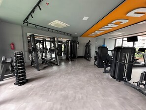 Une salle de sport équipée de divers appareils d’exercice, d’un extincteur et d’une grande fenêtre.