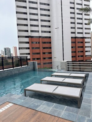 Zona de piscina al terrat amb gandules i vista d'un edifici de grans alçades.