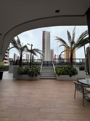 A rooftop terrace with a view of tall buildings, a staircase, and palm trees. - Cozy 1-bedroom apartment in marvelous Fortaleza with AC and gym (Fortaleza)