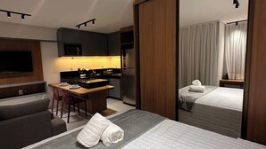 Moderni hotellihuone, jossa on sänky, sohva, ruokailutila ja keittiö.