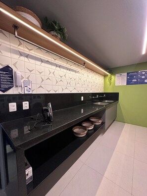 A modern kitchen with a black countertop, white patterned backsplash, and a green accent wall. - Cozy 1-bedroom apartment in marvelous Fortaleza with AC and gym (Fortaleza)