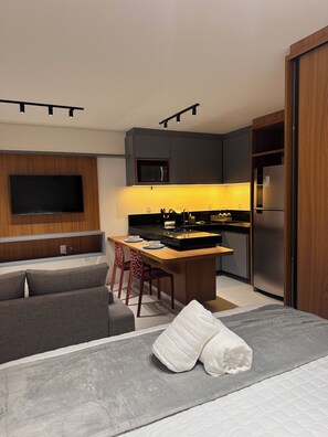 Une chambre d’hôtel moderne équipée d’un téléviseur à écran plat, d’une kitchenette, d’un coin repas et d’un lit.