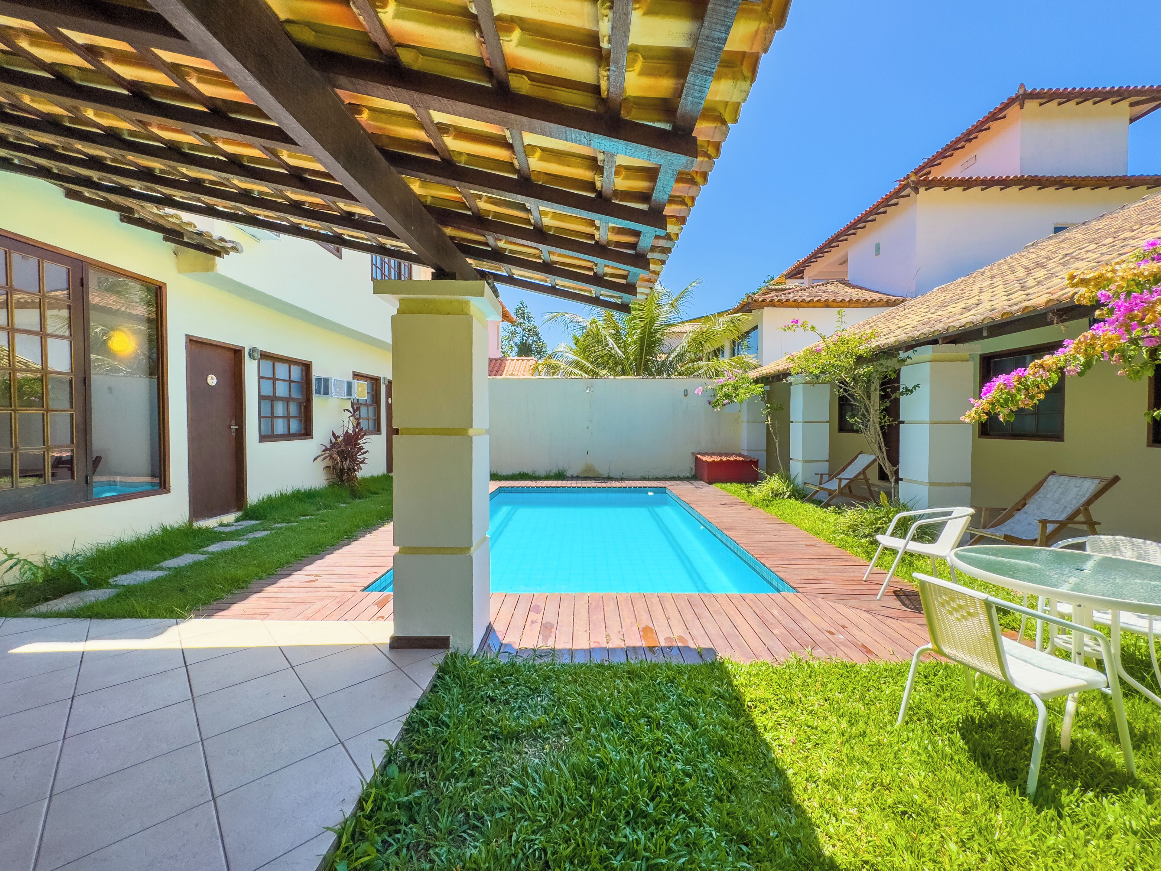 A swimming pool with a pergola overhead, surrounded by a patio area with chairs and a small garden.