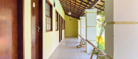 Un pasillo con puertas y ventanas de madera, suelo de baldosas y techo con vigas de madera y una lámpara colgante.