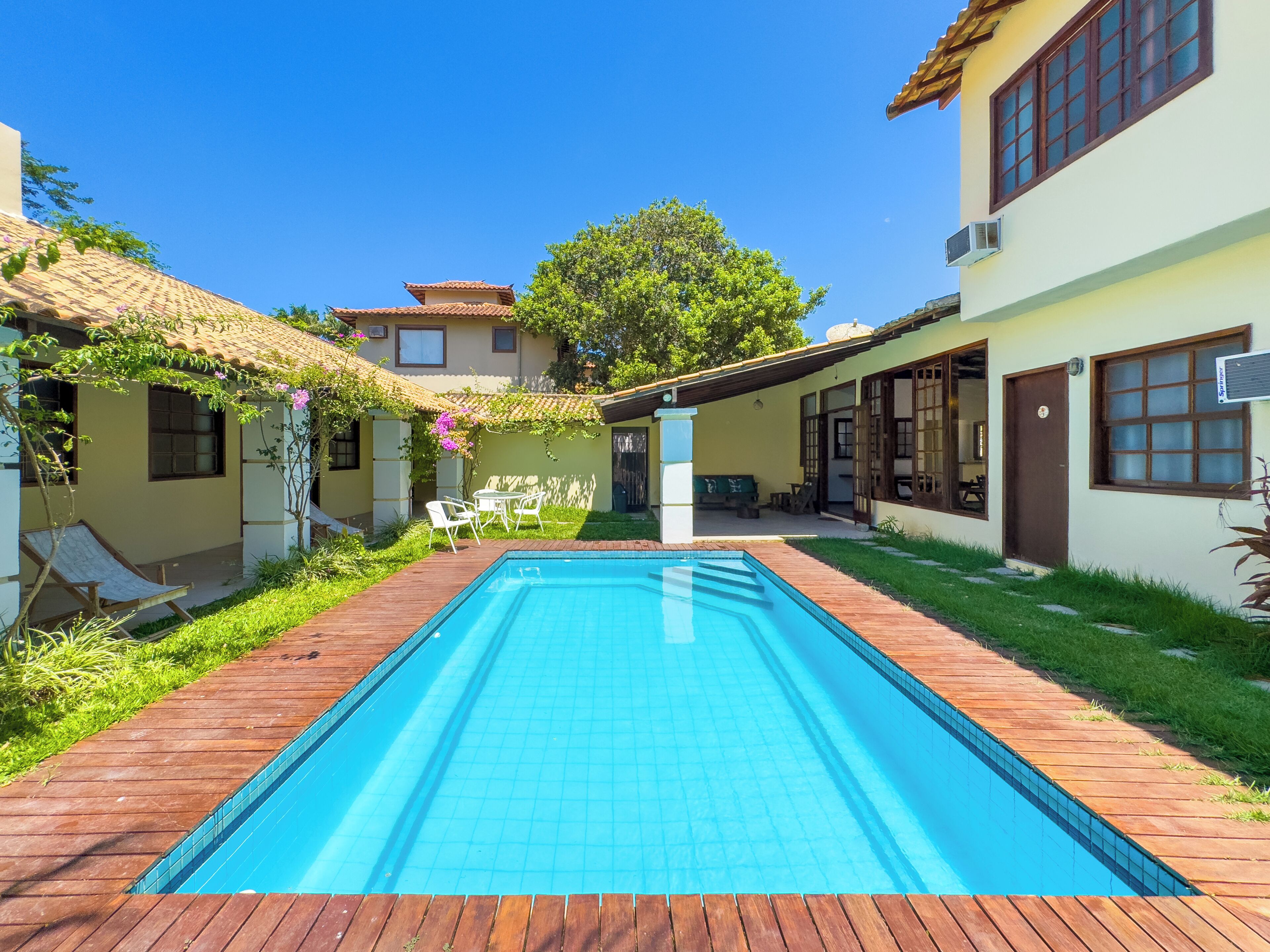 A swimming pool with a wooden deck, a patio with outdoor furniture, and a building with a tiled roof.