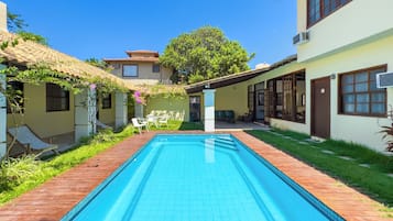 A swimming pool with a wooden deck, a patio with outdoor furniture, and a building with a tiled roof.