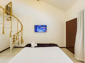 Une chambre d’hôtel avec un lit, un téléviseur fixé au mur, une porte en bois et un rideau blanc.