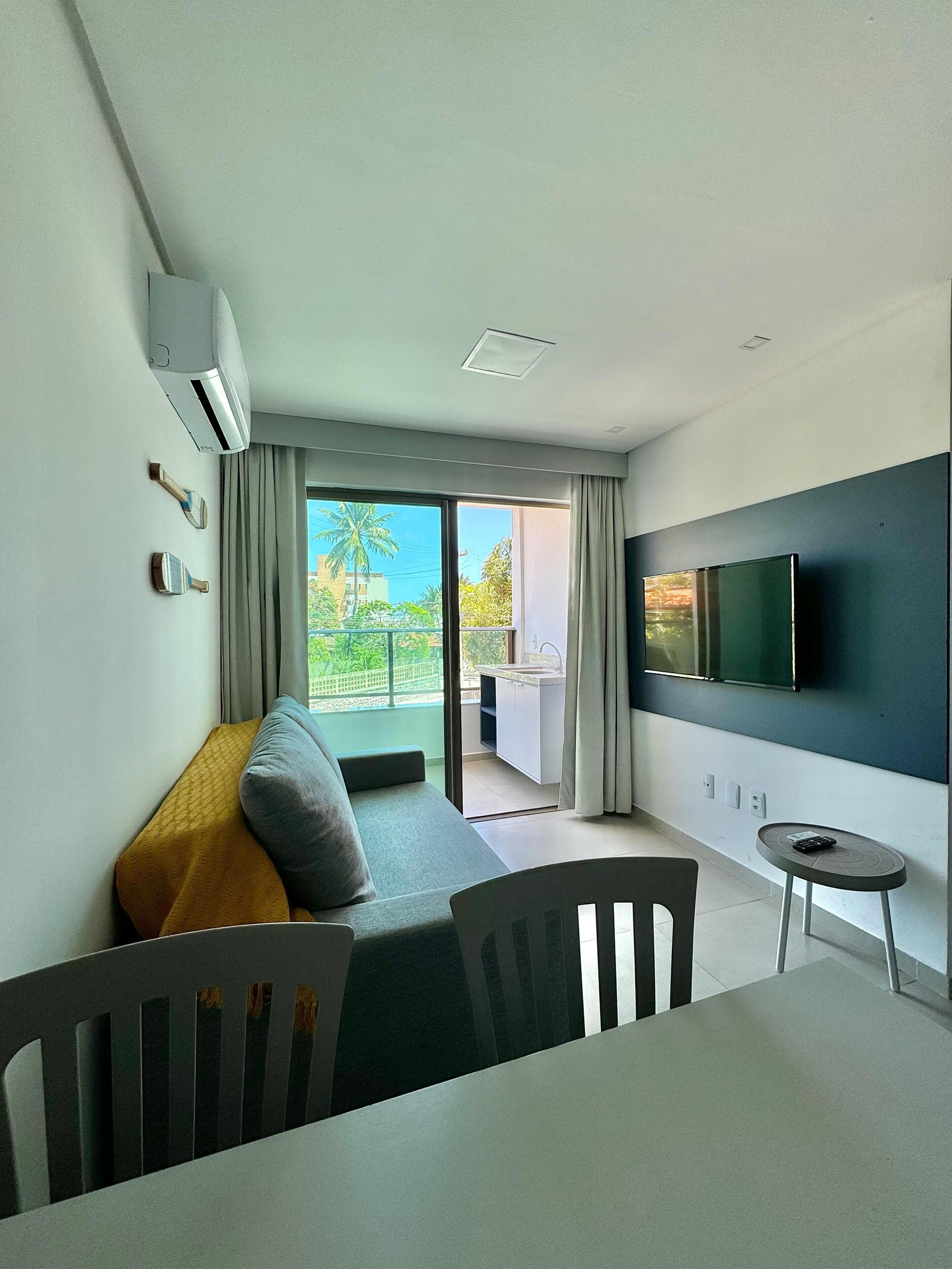 A modern hotel room with a sofa, a small table, a TV, and a balcony with a view.