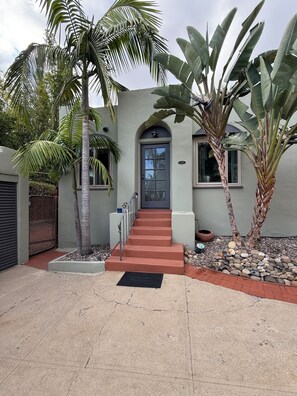 A house with a grey facade, a red staircase, and a palm tree in the front yard. - Casa Consuelo - 1926 Spanish Casita + Private Yard + Parking (San Diego)