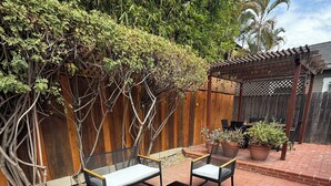 An outdoor patio area with a wooden pergola, two black metal chairs with cushions, and a small table. - Charming Furnished Casita with Private Yard in South Park/Golden Hill (San Diego)