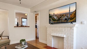 A living room with a fireplace, a ceiling fan, a television mounted above it, and a dining table with a plant. - Charming Furnished Casita with Private Yard in South Park/Golden Hill (San Diego)
