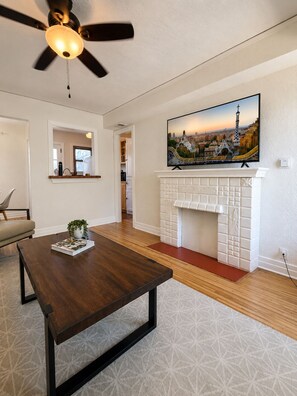 A living room with a fireplace, a ceiling fan, a television mounted above it, and a dining table with a plant. - Charming Furnished Casita with Private Yard in South Park/Golden Hill (San Diego)