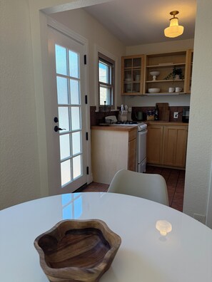 A kitchen with a white table, wooden cabinets, and a window. - Casa Consuelo - 1926 Spanish Casita + Private Yard + Parking (San Diego)