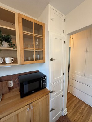 A kitchen with wooden cabinets, a microwave, and a white door. - Casa Consuelo - 1926 Spanish Casita + Private Yard + Parking (San Diego)