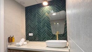 A modern bathroom with a herringbone-patterned wall, a white sink, and a wooden vanity. - La Casona de les Arts 1 - Oceanográfic (València)