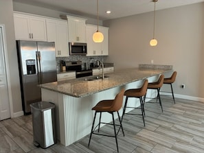 A modern kitchen with a stainless steel refrigerator, a microwave, and a granite countertop island with bar stools. - Themed Rooms 4 BD/ 3 BA/ Storey Lake - 3083 PP (Kissimmee)