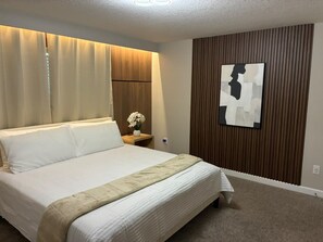 A hotel room with a large bed, a nightstand with a vase of flowers, a wooden panel wall, and a piece of abstract art. - Themed Rooms 4 BD/ 3 BA/ Storey Lake - 3083 PP (Kissimmee)