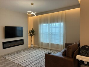 A modern living room with a flat-screen TV, a fireplace, a large window with sheer curtains, and a brown sofa. - Themed Rooms 4 BD/ 3 BA/ Storey Lake - 3083 PP (Kissimmee)