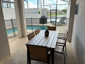 An outdoor patio with a pool, wooden table, chairs, and a grill. - Themed Rooms 4 BD/ 3 BA/ Storey Lake - 3083 PP (Kissimmee)