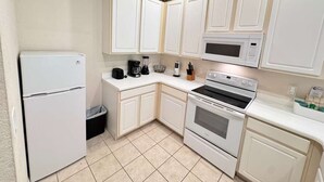 Una cocina compacta con alacenas blancas, un refrigerador, un microondas y un horno.