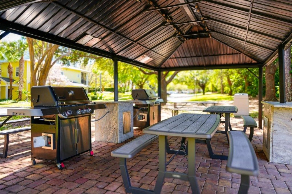 En udendørs terrasse med et overdækket område, to grill og picnicborde.