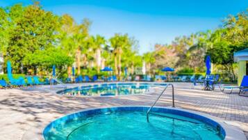 A swimming pool with a hot tub, surrounded by lounge chairs and umbrellas.