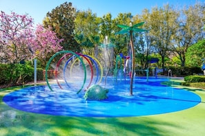Ein Wasserspielbereich mit einer blauen, kreisförmigen Oberfläche, bunten Ringen und einer grünen Schildkrötenstatue.