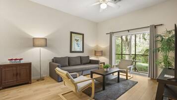A living room with a sofa, armchair, coffee table, and a ceiling fan.